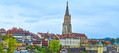 Bern Minster Katedrali 'nin yüksek taş çan kulesi. İsviçre' nin Bern kentindeki evlerin çatıları üzerinde.