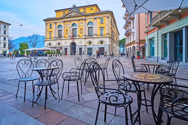The small tables and chairs of the outdoor dining on Piazza della Riforma against Palazzo Civico building, Lugano, Switzerland
