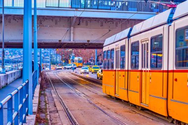 Jane Haining rıhtımında akşam trafiği sırasında sarı tramvay ve arabalı şehir manzarası, Budapeşte, Macaristan