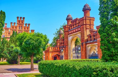 Chernivtsi Ulusal Üniversitesi 'nin yemyeşil bahçesinin arkasındaki zengin dekore edilmiş tuğla kapı, Ukrayna