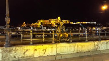 Macaristan 'ın başkenti Budapeşte' de, nehrin karşı kıyısındaki tepenin üstünde küçük prenses heykeli, Tuna Nehri ve Buda Kalesi manzaralı eski Pest bölgesinde akşam yürüyüşü