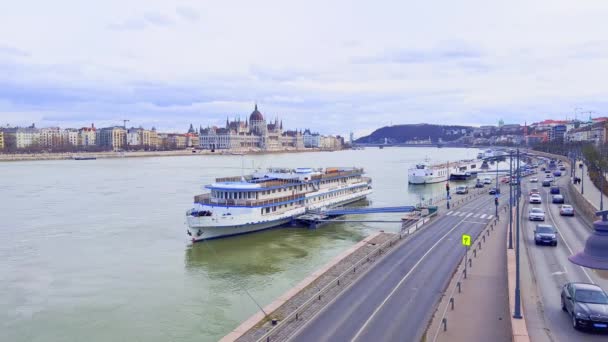 ブダペスト ハンガリーのアンジェロ ロッタ堤防の背景とトラフィックでゴシック議会の建物のビューでドナウ川の銀行で係留されています — ストック動画