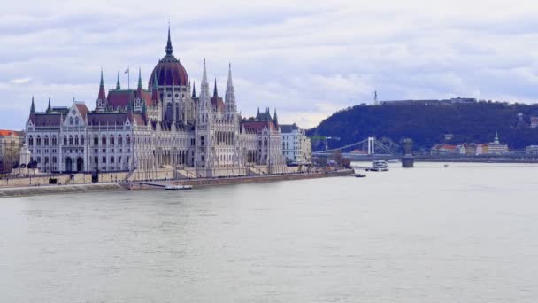 ドナウ川に面した歴史的なゴシック様式の議会の建物で バックグラウンド ブダペスト ハンガリーのゲラートヒルを眺めることができます — ストック動画