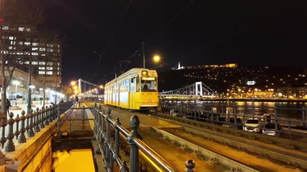 レトロイエローのトラムは ブダペスト ハンガリーの夕方の都市でエリザベス橋に乗ります — ストック動画