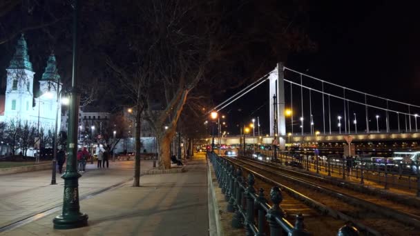ハンガリー ブダペスト ハンガリーの背景にある乗馬の黄色いトラム シティパリッシュ教会 エリザベス橋の景色を望む夜のジェーン ヘイン エンバンクメント — ストック動画