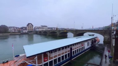 Ren Nehri manzaralı Basel 'de karlı hava, demirli gemi ve tarihi taş kemerli Mittlere Brucke (Orta Köprü), İsviçre