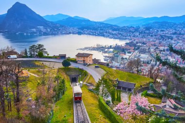 The cloudy evening sky over Monte San Salvatore, Lake Lugano and Monte Bre funicular, seen from Albonago village viewpoint on the slope of Monte Bre, Ticino, Switzerland clipart