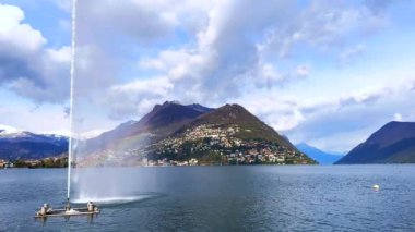 Lugano Gölü 'ndeki Getto d' Acqua (Lugano Körfezi 'ndeki Su Jeti) fıskiyesi ayaklarında parlak bir gökkuşağı ve arka planda Alp manzarası olan Lugano, Ticino, İsviçre