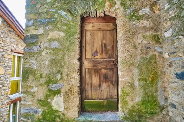 Yeşil yosunlarla kaplı ortaçağ taş ev duvarı ve paslı kilidi olan eski ahşap kapı, Bre, Ticino, İsviçre