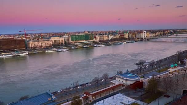 ダヌーブ川 紫の空 ペスト地区 ブダペスト ハンガリーの建物の橋を望むブダ城の丘からの夕暮れのタイムラプスパノラマ — ストック動画