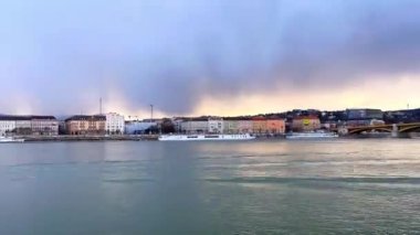 Tuna Nehri üzerinde ve Macaristan 'ın Budapeşte kentinin tarihi mahallelerinde günbatımı gökyüzünde alçak fırtınalı bulutların yer aldığı zaman panoraması