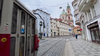 Mala Strana 'daki Karmelitska Caddesi' ndeki klasik kırmızı tramvay tarihi evlerin arkasındaki Aziz Nicholas Kilisesi 'nin kubbe ve kuleleri manzaralı, Prag, Çek Cumhuriyeti