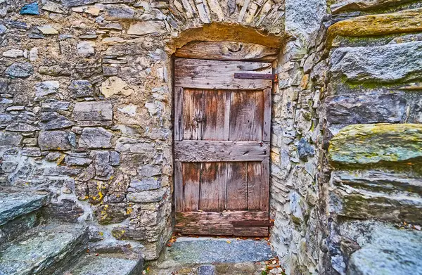 The wall of the medieval stone house and the vintage wooden door in mountain village of Bre, Switzerland