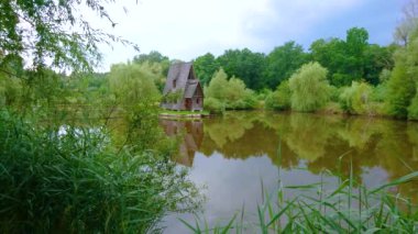 Küçük gölün ayna benzeri yüzeyi, yemyeşil ormanı ve Ukrayna 'nın Lviv Bölgesi, Zbrui Köyü' ndeki Styr av çiftliğinde bulunan küçük avcının evini yansıtır.
