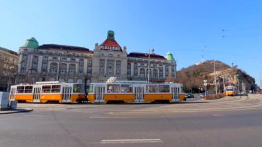 St. Gellert Meydanı 'nda hızlı trafik ve Gellert Oteli ve Termal Hamamlar, Budapeşte, Macaristan' a karşı klasik sarı tramvay sürüyor.