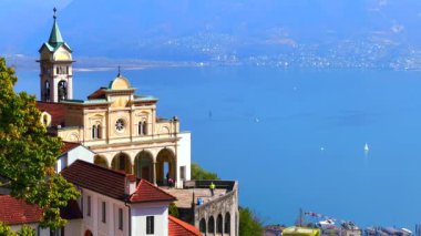 Madonna del Sasso Sığınağı Santa Maria Assunta Kilisesi 'nin cephesi Maggiore Gölü, Orselina, İsviçre' nin parlak mavi yüzeyine karşıdır.