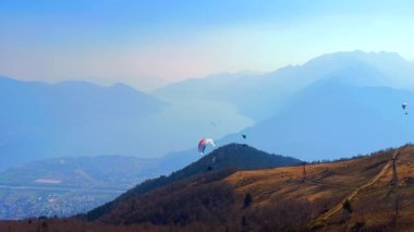 Vadideki Maggiore Gölü ve dağların üzerinden uçan renkli planörlü uçaklarla sisli Alp manzarasının tadını çıkarın. Cimetta Dağı, Ticino, İsviçre