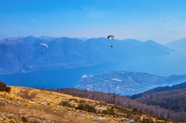 Maggiore Gölü ve İsviçre 'nin Ticino Dağı yamacında planör uçaklarıyla manzaralı dağ manzarası.