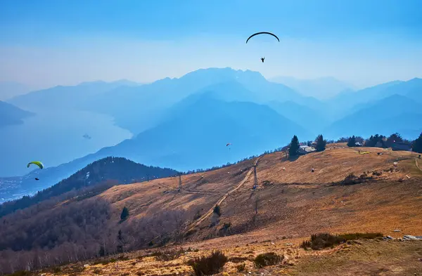 The sunny hazy day on Cimetta Mount with a view of the glider aircrafts, flying over the mountain slopes, Ticino, Switzerland