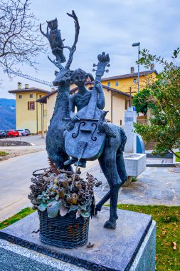 COLLINA D 'ORO, SWitzERLAND - 18 Mart 2022: 18 Mart' ta İsviçre 'nin Collina d' Oro kentinde geyiğin üzerinde oturan ve çello çalan kızın modern heykeli