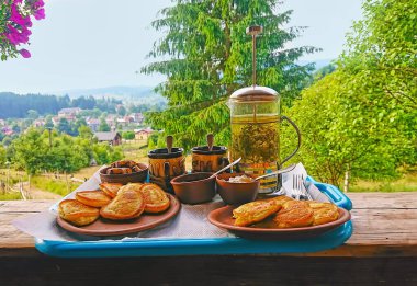 The tray with homemade pancakes and herbal tea on the terrace of the house in mountain forest, Carpathians, Ukraine clipart