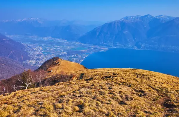 stock image The dried up yellow Cardada Cimetta slope and Alpe Cardada against the hazy mountain valley with Lake Maggiore and Alps in the background, Ticino, Switzerland