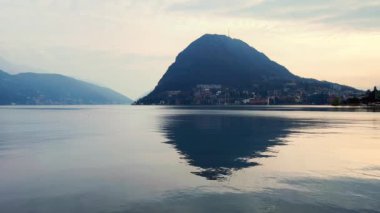 Monte San Salvadore 'un karanlık akşam siluetinin ardındaki bulutlu gökyüzü Lugano Gölü' nün yüzeyine yansıyor, Lugano, İsviçre