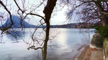 Lugano Gölü 'nün manzaralı manzarası çınar dallarından geçerek arka planda Monte San Salvatore, Lugano, Ticino, İsviçre