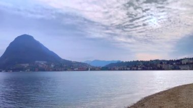 Lugano Gölü 'nde sisli bir bahar akşamı Monte San Salvatore, Monte Sighignola, Monte Bre, kıyıya demirlemiş yatlar ve İsviçre' nin dalgalı sularındaki martı sürüsü Lugano,