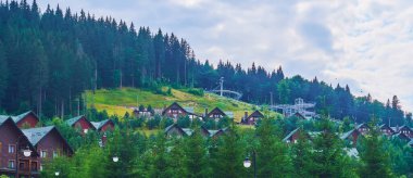 Karpatlar, Bukovel ve Ukrayna 'nın yüksek kozalaklı ormanlarını çevreleyen dağ yamacındaki ahşap bungalovların panoraması