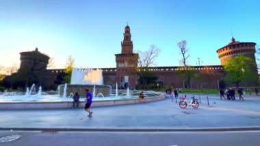 MILAN, ITALY - 9 Nisan 2022: Ortaçağ Sforza Kalesi 'nin önündeki tarihi Piazza Castello ve Castle Fountain, 9 Nisan akşamı Milano' da uzun Filarete Kulesi ve tuğla surlar