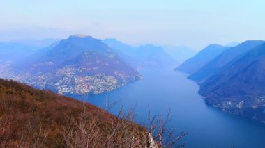 Monte San Salvatore 'un zirvesi Lugano Gölü, Monte Bre, Monte Boglia ve Lugano Prealps, Ticino, İsviçre' nin diğer puslu tepeleri ve yamaçlarında görülür.