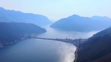 Monte San Salvatore, arka planda Melide Causeway ve Monte San Giorgio silueti, Ticino, İsviçre ile gök mavisi Lugano Gölü manzarasını açar.