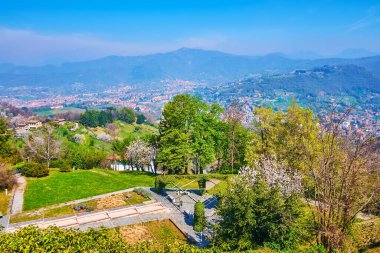 The hazy mountains from the top of San Vigilio Hill, covered with green and flowering spring trees, Bergamo, Italy