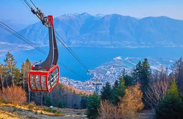 stock image The modern red Orselina Cardada Mount cable car against the Lake Maggiore and hazy Alps, a view from the slope of Cardada Cimetta, Ticino, Switzerland