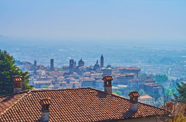 The medieval churches, bell towers and houses of Bergamo Alta behind the old tile roof on San Vigilio Hill, Bergamo, Italy clipart