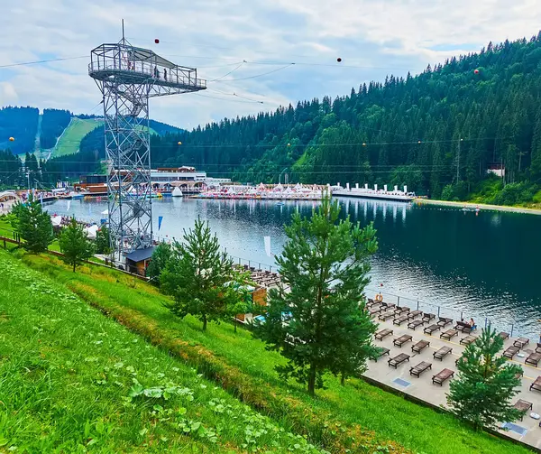 stock image The Molodist Lake with tower of zip line, sunbeds, tourist pavilions and green Carpathian Mountains, Bukovel, Ukraine