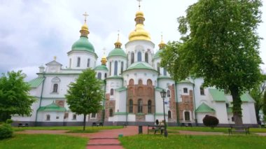 Aziz Sophia Katedrali 'nin manzaralı bahçesinde uzun kestane ağaçları ve yeşil çimlerle yürüyün, tarihi Katedral' in dış yüzünü maymunla ve kubbelerle izleyin, Kyiv, Ukrayna