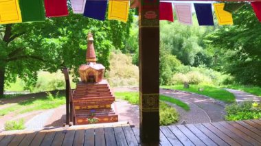 Kyiv Botanik Bahçesi 'nde renkli dua bayrakları ve arka planda küçük taş Chorten (stupa) ile süslenmiş kereste taraçalı yeşil Tibet Bahçesi manzarası, Ukrayna