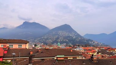 Monte Bre ve Monte Boglia üzerinde hızla akan bulutlar Lugano 'nun eski kiremit çatılarıyla, Ticino, İsviçre