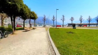 Giardini Jean Arp (bahçe) boyunca Maggiore Gölü 'nün Lungolago Giuseppe Motta rıhtımına küçük tekneleri, yatları, turistik feribotları ve Alpler, Locarno, İsviçre manzarası ile birlikte yürür.