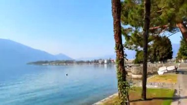Zaman çizelgesi, yeşil parklar ve puslu Alpler, Locarno, İsviçre ile çevrili Maggiore Gölü boyunca yürüyor.
