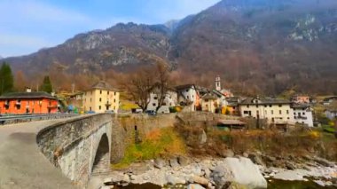 Zaman çizelgesi, Maggia Nehri 'nin karşısındaki eski taş köprüden geçerek ortaçağ Prato Sornico köyü Val Lavizzara, Vallemaggia, Ticino, İsviçre' ye yürür.