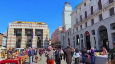 Arka planda Postane Sarayı ve Torre della Rivoluzione (Devrim Kulesi) ile birlikte Piazza della Vittoria 'nın (Zafer Meydanı) ortasında bulunan kalabalık bit pazarı geçidi, Brescia, İtalya