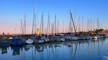 The line of the moored sail yachts in Port with a lighthouse and sunset sky in background, Desenzano del Garda, Lake Garda, Italy
