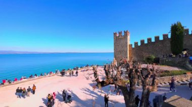 Scaligero Kalesi 'nin ortaçağ kuleleri ve duvarları önünde Garda Gölü' nde kalabalık bir halk plajı olan Sirmione, İtalya