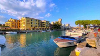 The tourist and fishing boats in a small marina of Sirmione, located next to the old town with a view on hotels, colored houses and towers of Scaligero Castle, Lombardy, Italy