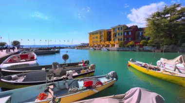 The colored fishing and tourist boats in marina of Sirmione, located next to the old town and facing traditional houses and villas, Lombardy, Italy