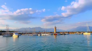 The evening panorama of the port in Desenzano del Garda on Lake Garda with moored yachts, small boats, old stone lighthouse and embankment of old town, Italy