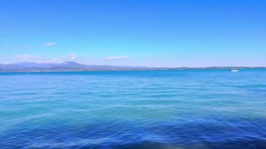 Scaligero Kalesi 'nin ortaçağ duvarlı parlak mavi Garda Gölü Panoraması, dalgalı göl yüzeyinin arkasındaki Garda Prealps siluetleri, Sirmione, İtalya
